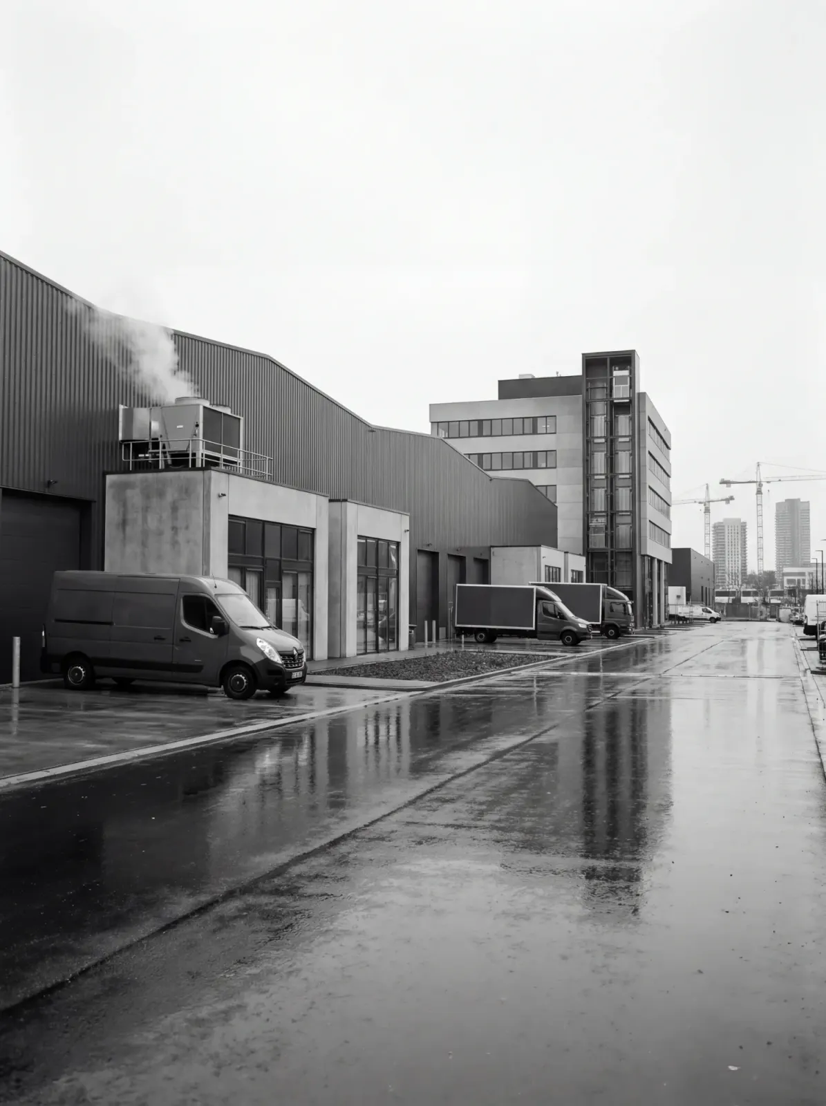 Bestelbus voor een bedrijfspand in de regen, met op de achtergrond een gebouw met glazen liftschacht